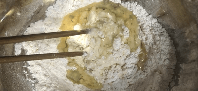 搅拌至面粉成絮状,然后将黑芝麻倒进去,揉面团至均匀状,盖上保鲜膜,醒