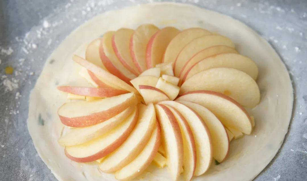 5,将苹果片呈散开状铺在饼皮奶酪丁的上方,同样预留出边缘.