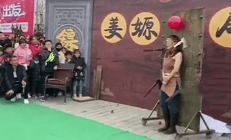湖南一男子表演扔飞斧，女子站木板前紧张躲闪，观众捏把汗