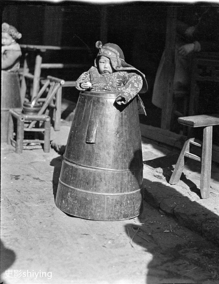 小朋友被放在了一个装粮食的厚重的大木桶中,仔细看他的手里,好像还拿