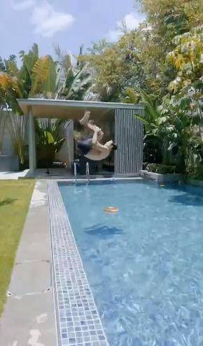 田亮穿着泳裤,站在游泳池旁边,平地后空翻入水,而且水里还放着一个小