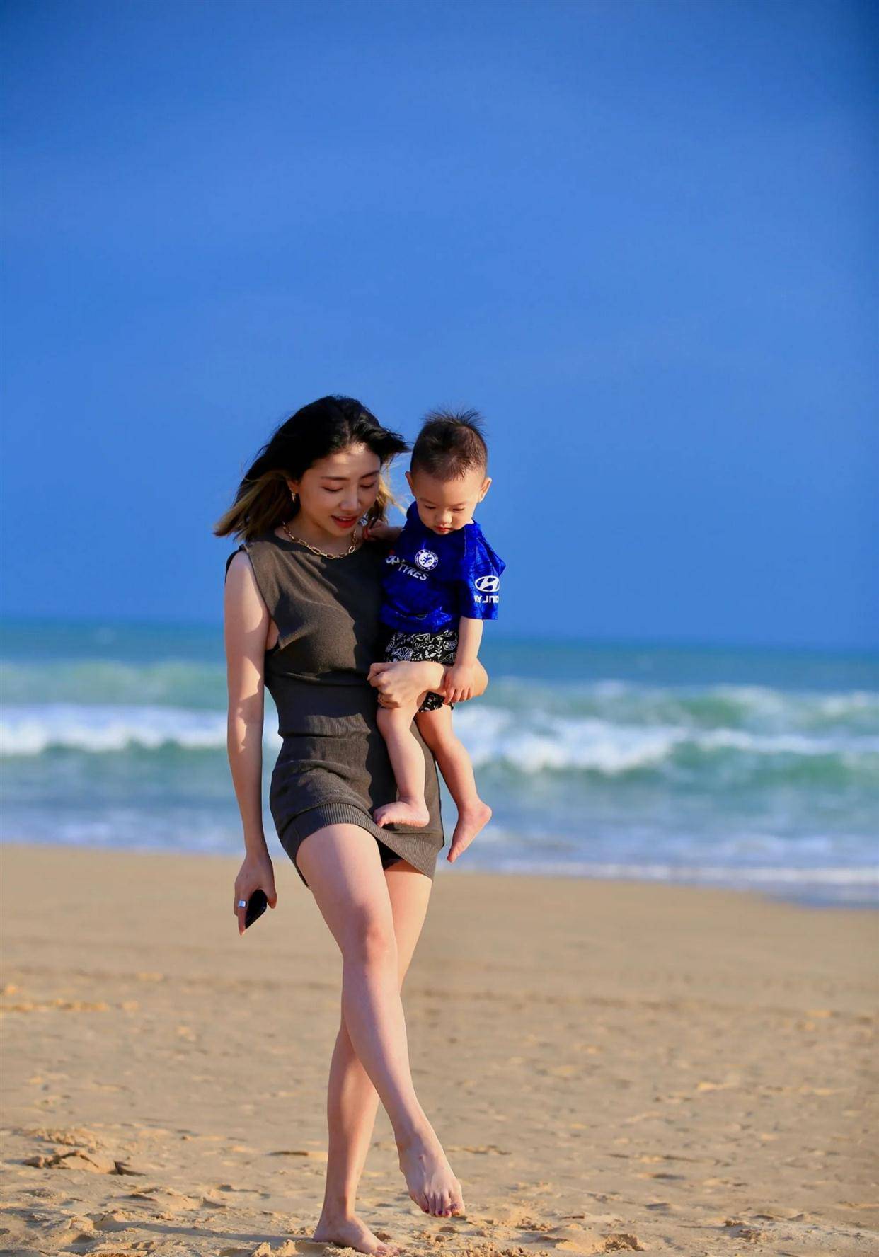 周捷光着脚走在海滩中,无袖的连衣裙更加突出胳膊的纤细感,在搭配一双