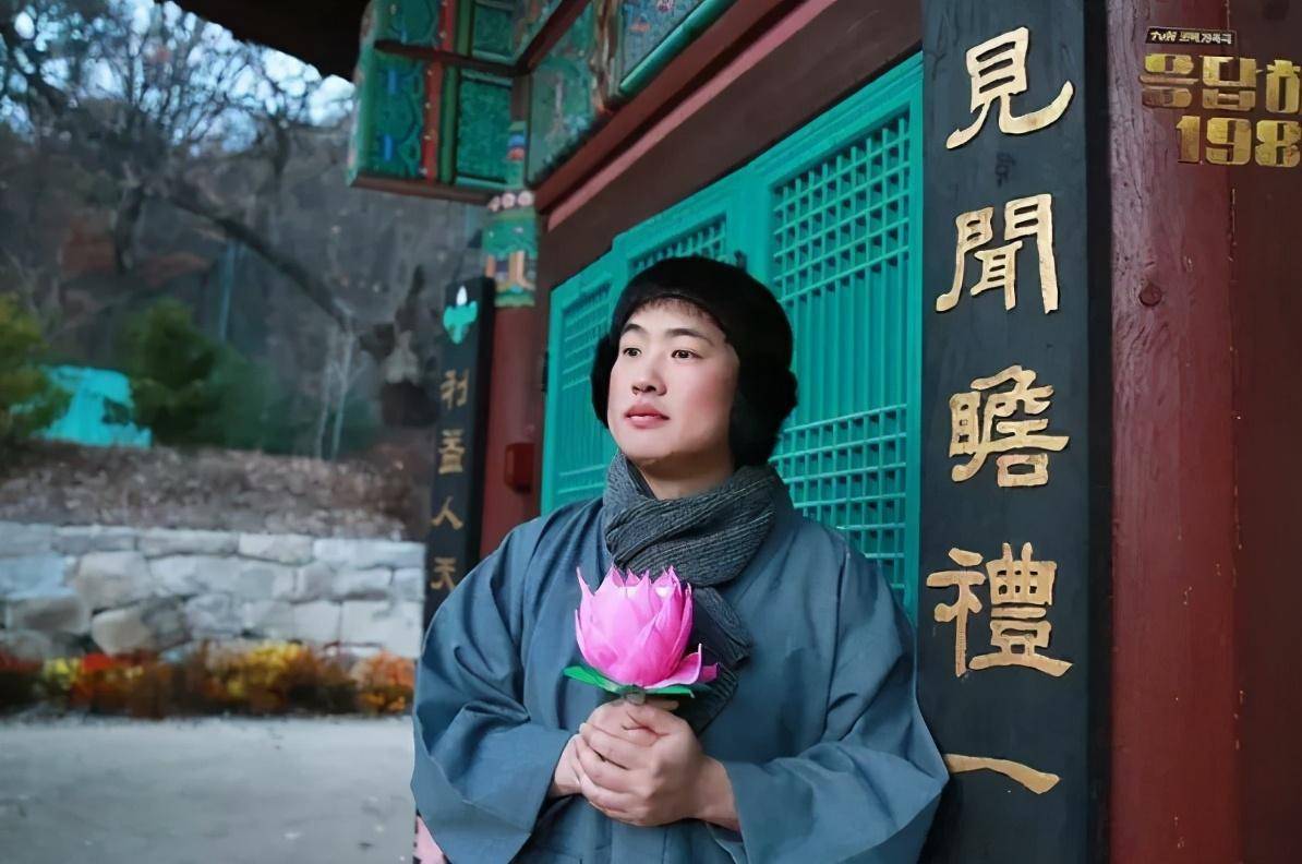 只见他手握荷花,满脸平静地站在寺庙前,感觉已经心无旁骛,不与世俗同