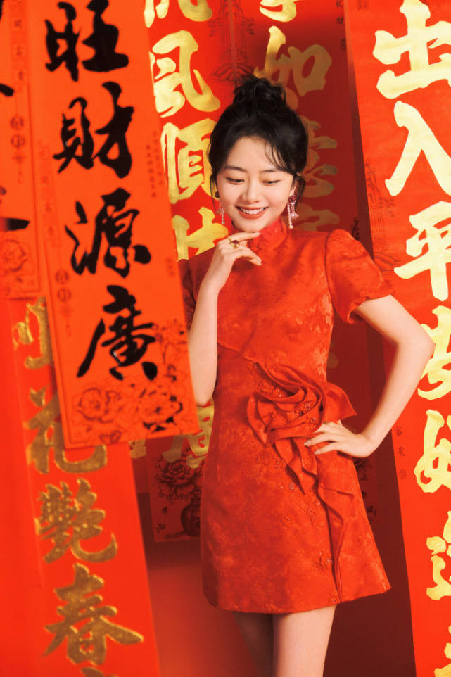 画面中的谭松韵身穿大红色的旗袍款连衣裙,手中拿着写有"新年快乐"的