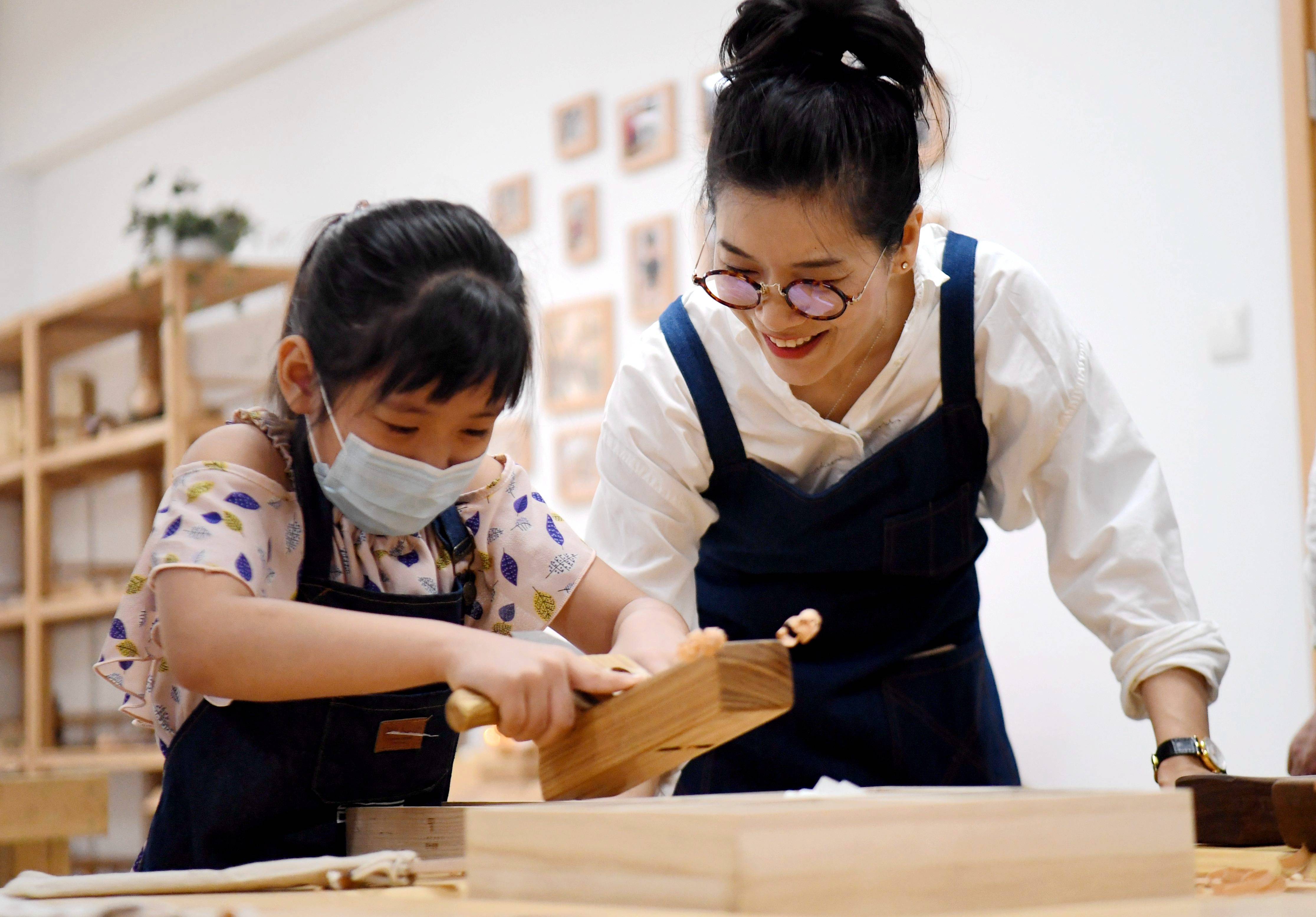 7月31日,一名小朋友在木工老师指导下使用刨子.