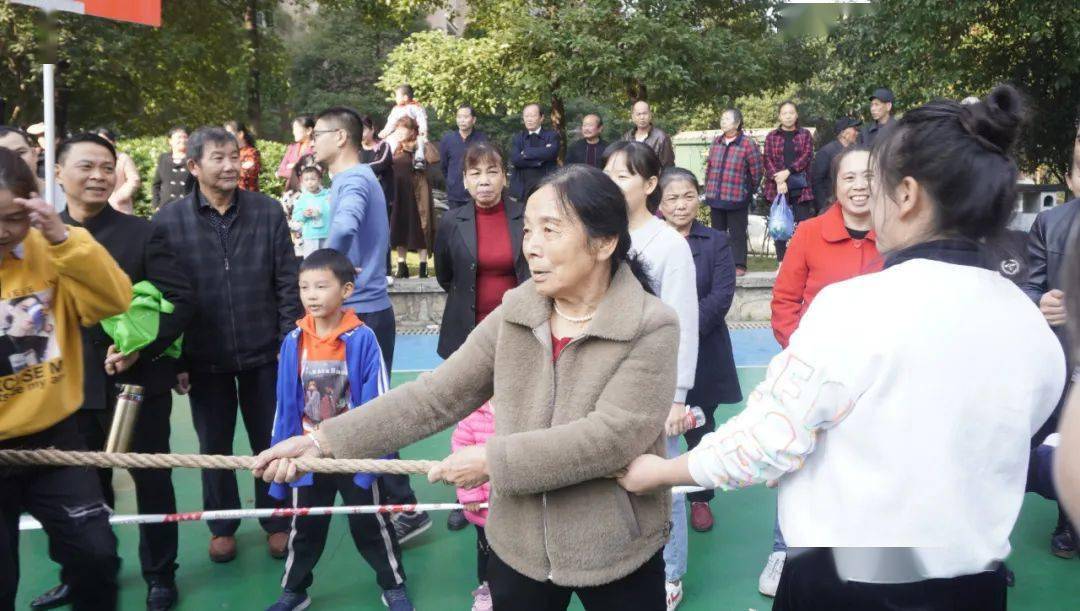 在一支由精壮男子组成的拔河队伍中,一名70岁的奶奶穿着棕色呢子衣,梳