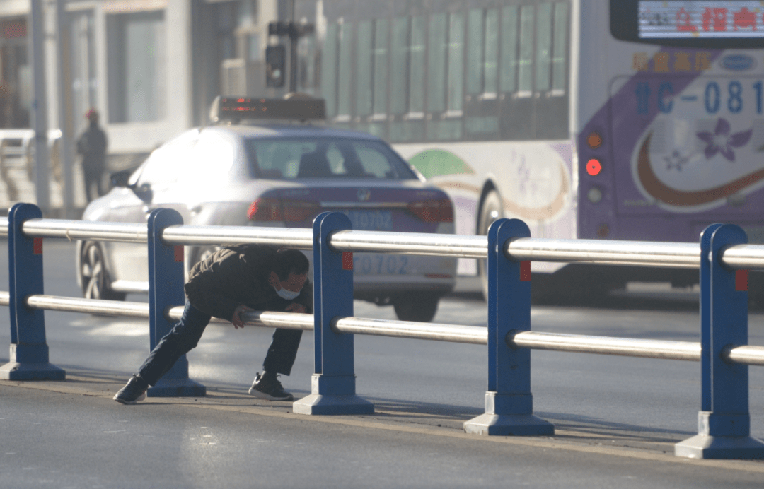 两名行人在紫金广场对面翻越栏杆,下面就是人行通道.