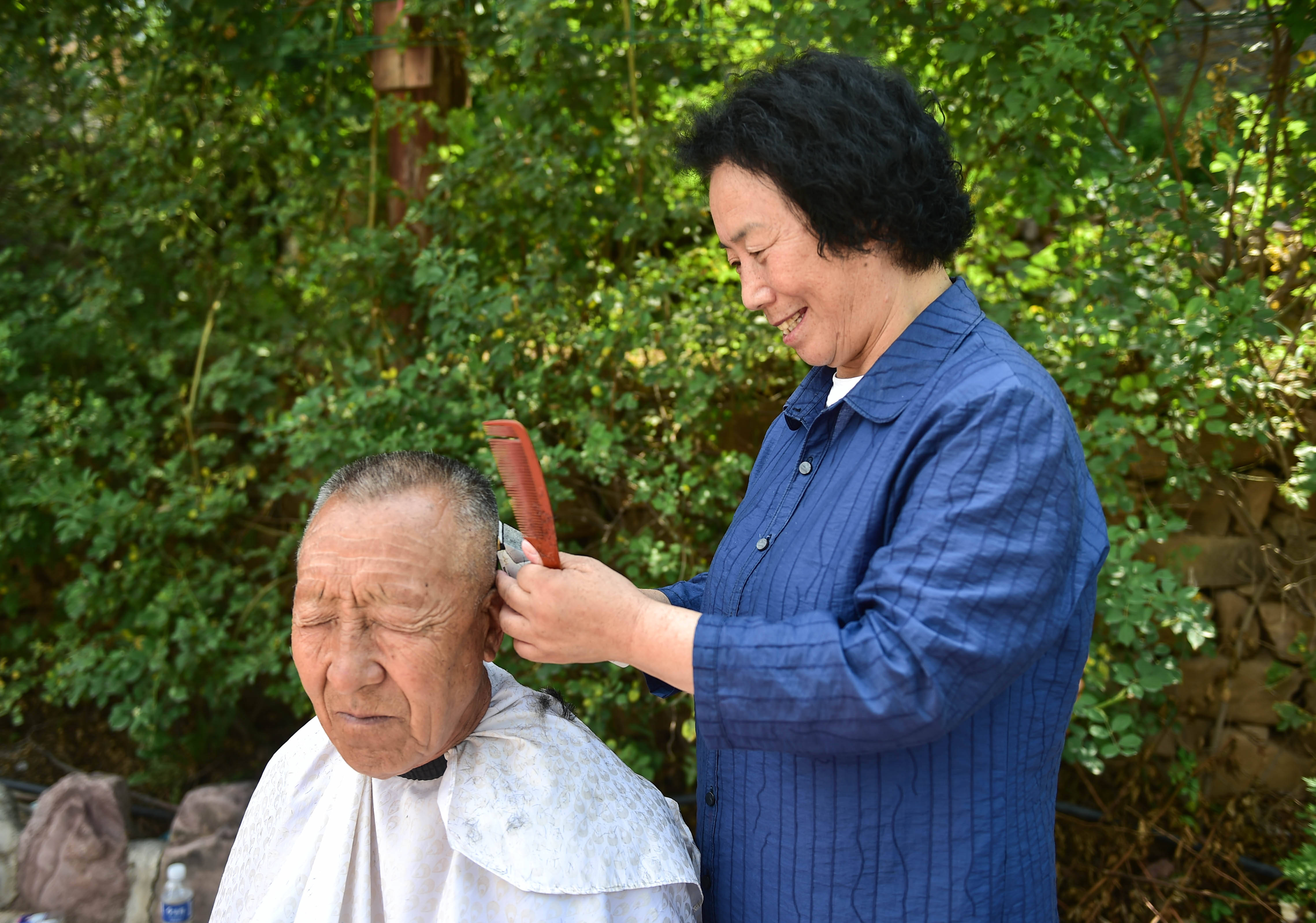 7月7日,在山西省阳城县东哄哄村,栗红连(右)给村里的老人理发