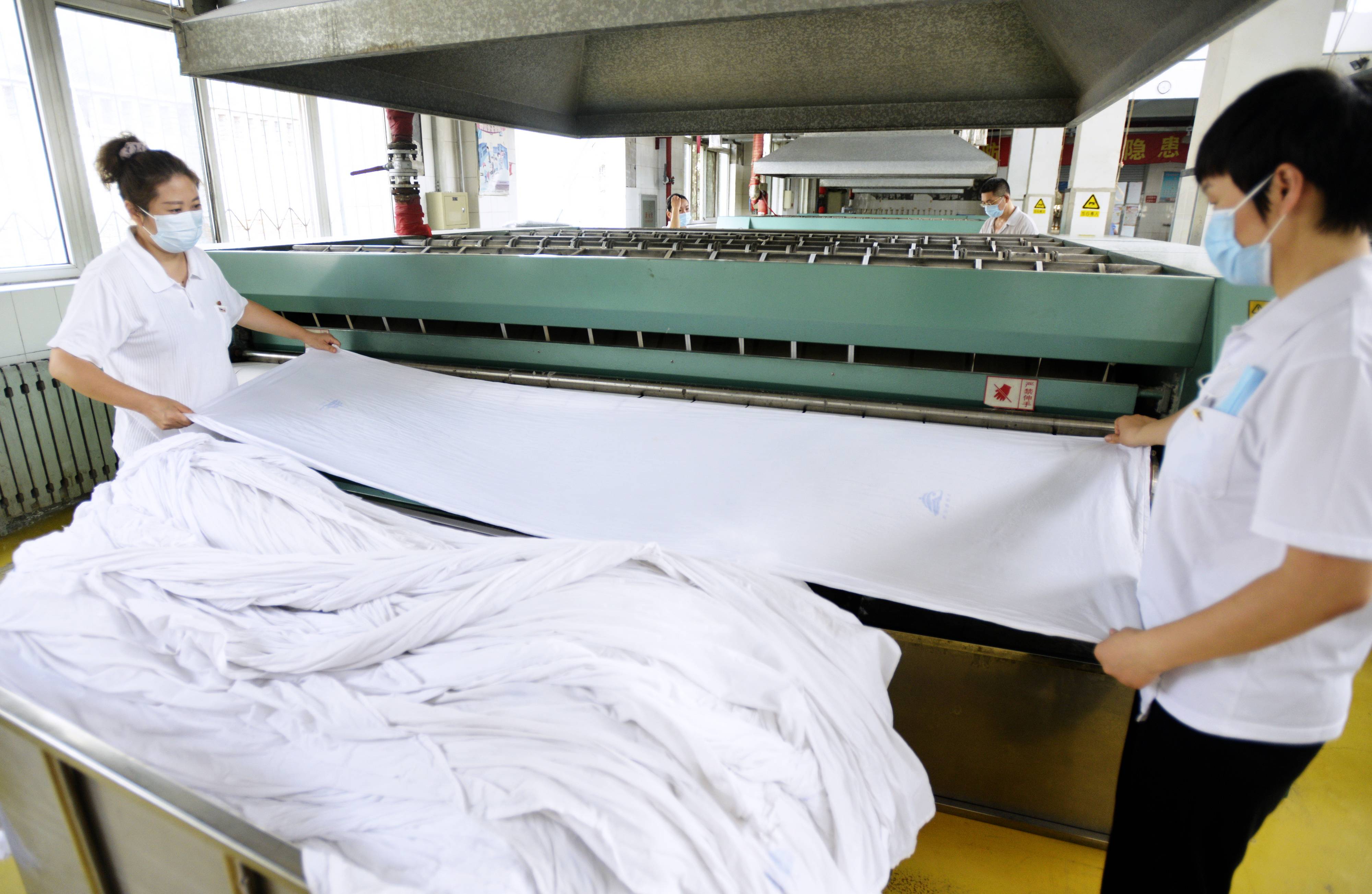 8月23日,北京客运段洗涤车间的工作人员在对洗涤后的卧具进行高温熨烫