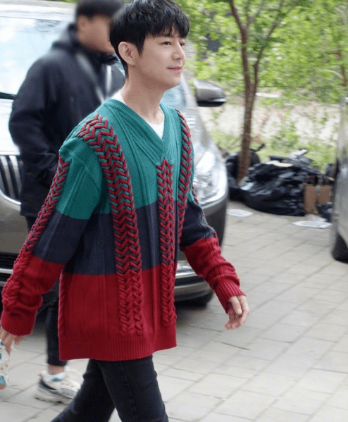 何炅衣着一件时髦的毛衣,红蓝绿三色搭配,脚踩运动鞋,下身搭配一件破